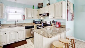 Una cocina moderna con armarios blancos, encimeras de granito, una isla central con taburetes, lavavajillas, estufa y microondas.