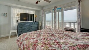 A bedroom with a bed, a dresser, a television, and a balcony with a view of the ocean. - Oceanfront Duplex with unobstructed ocean views! (North Topsail Beach)