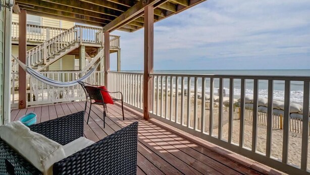 A wooden deck with wicker furniture, a hammock, and a staircase leading to an upper level. - Oceanfront Duplex with unobstructed ocean views! (North Topsail Beach)