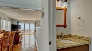 A modern interior with a wooden floor, a dining area with chairs, a sofa, and a TV. There's a large window with a view of the outdoors. - Oceanfront Duplex with unobstructed ocean views! (North Topsail Beach)