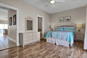A bedroom with a wooden floor, a bed with patterned bedding, a dresser, and two wall-mounted lamps. - Unobstructed Ocean Views!  4 Bedroom townhouse, beach access, community pool (Surf City)