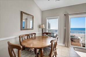 A dining area with a wooden table and chairs, a mirror on the wall, a window with blinds, and a view of the ocean. - Unobstructed Ocean Views!  4 Bedroom townhouse, beach access, community pool (Surf City)
