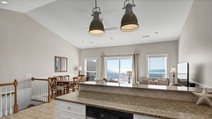 A spacious kitchen with a large island, a dining area with wooden chairs, and a view of the ocean through large windows. - Unobstructed Ocean Views!  4 Bedroom townhouse, beach access, community pool (Surf City)