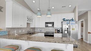 A modern kitchen with white cabinets, a granite countertop, a stainless steel refrigerator, and a coffee maker. - Unobstructed Ocean Views!  4 Bedroom townhouse, beach access, community pool (Surf City)