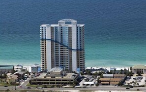A high-rise hotel with multiple floors, a parking area, and a view of the ocean.