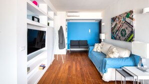 A modern living room with a blue sofa, a flat-screen TV, a white desk, and a wall-mounted artwork. - Vista sulle Cupole by Wonderful Italy (Palermo)
