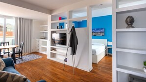 A modern hotel room with a wooden floor, a dining area with a table and chairs, a bed with a white headboard, and built-in shelving with various items. - Vista sulle Cupole by Wonderful Italy (Palermo)