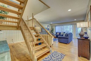 Un salon spacieux avec un escalier en bois, un canapé bleu et une grande fenêtre avec des rideaux.