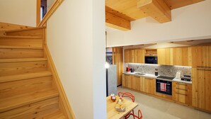 Una cocina moderna con armarios de madera, una zona de comedor con mesa y sillas, y una escalera de madera.