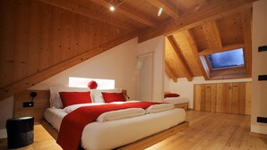 Un dormitorio con techo inclinado, vigas de madera, cama con ropa de cama roja y blanca, una ventana y un radiador.