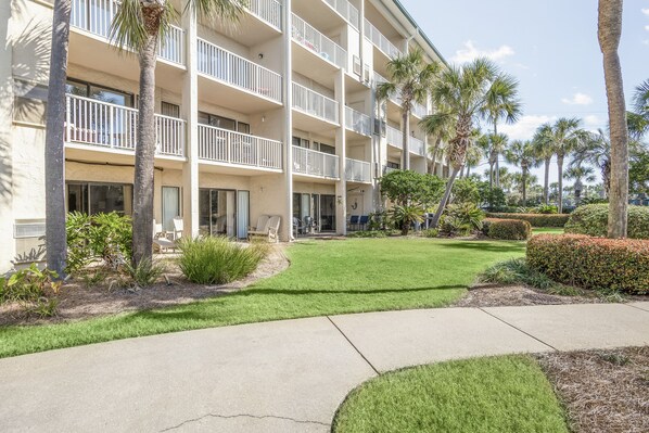 A multi-story hotel with balconies, palm trees, and a well-maintained lawn.