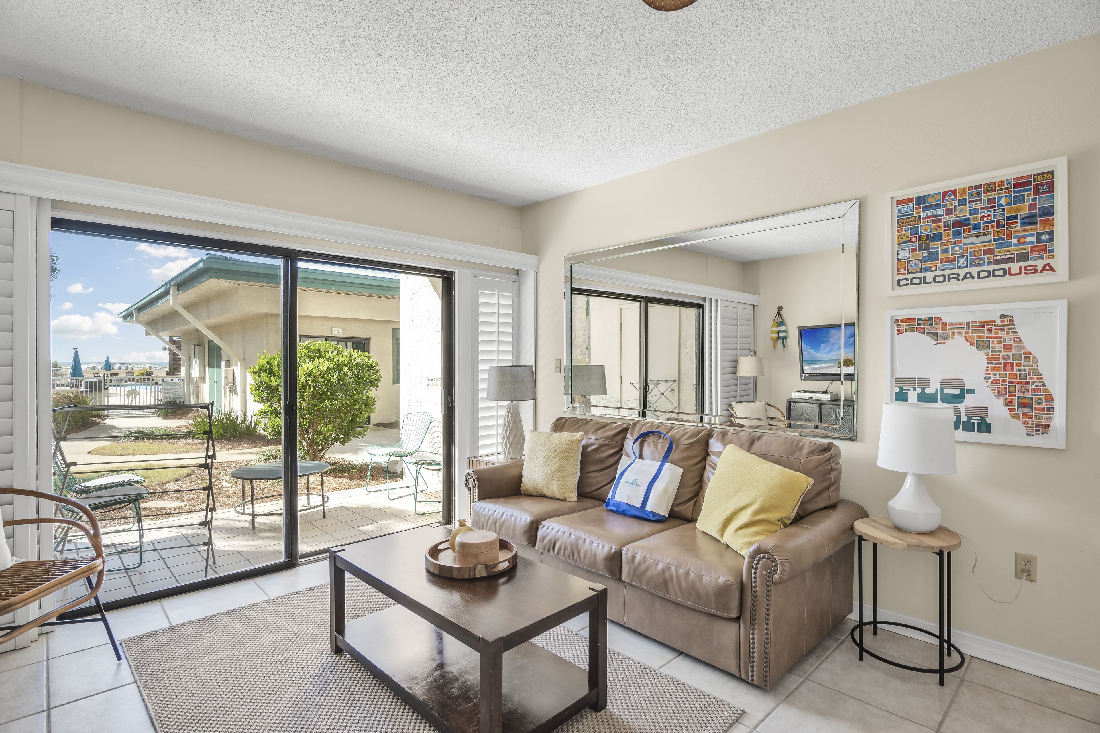A living room with a sliding glass door leading to a patio, a brown leather sofa, a coffee table, and a small side table with a lamp.
