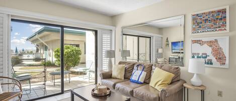 A living room with a sliding glass door leading to a patio, a brown leather sofa, a coffee table, and a small side table with a lamp.