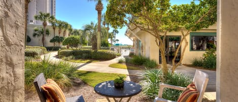 A patio area with two chairs and a small table, surrounded by palm trees and a well-maintained garden.