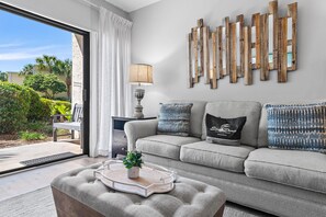 Ein modernes Wohnzimmer mit grauem Sofa, einem Couchtisch mit Pflanze, einem Beistelltisch mit Lampe und einem dekorativen Holzbild an der Wand.
