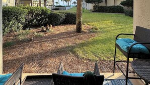 A patio with wicker furniture, a grassy lawn, and palm trees.