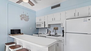 A kitchen with white cabinets, a microwave, a refrigerator, and a bar stool area.