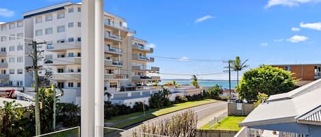 Un edificio residenziale a più piani con balconi, vista libera sul mare e una strada alberata con una recinzione.