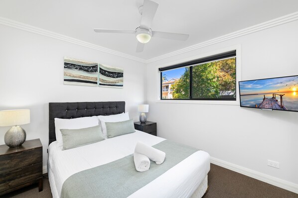 A bedroom with a bed, a nightstand, a lamp, a ceiling fan, and artwork on the walls.