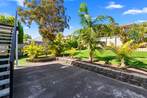 A paved driveway leading to a house with a stone retaining wall and a grassy lawn.