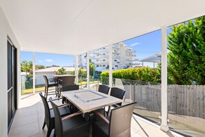 Un balcon avec une table et des chaises, de grandes fenêtres et une vue sur un quartier résidentiel.