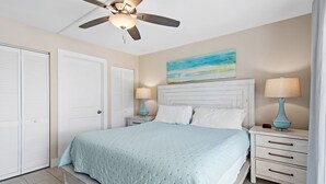 A bedroom with a bed, nightstands, a ceiling fan, and a painting on the wall. - Newly Renovated, unit 20 right on Beach… Just steps to the Sand (Destin)