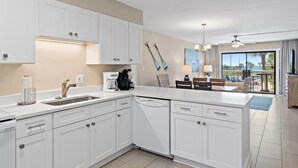 A modern kitchen with white cabinetry, a dishwasher, and a dining area with a table and chairs. - Newly Renovated, unit 20 right on Beach… Just steps to the Sand (Destin)