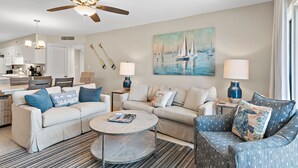 A living room with a ceiling fan, two sofas, a coffee table, and a painting of sailboats on the wall. - Newly Renovated, unit 20 right on Beach… Just steps to the Sand (Destin)