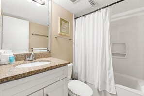 Une salle de bain équipée d’un lavabo, d’un miroir, d’un porte-serviettes, de toilettes et d’un rideau de douche.