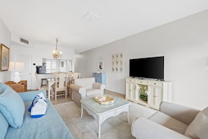 Sala de estar com sofá, mesa de centro, televisão e área de jantar com cadeiras e mesa.