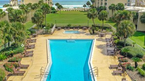 A swimming pool with lounge chairs, surrounded by palm trees and a view of the ocean. - Beach-side, beautiful low-rise with uncrowded beach! (Destin)