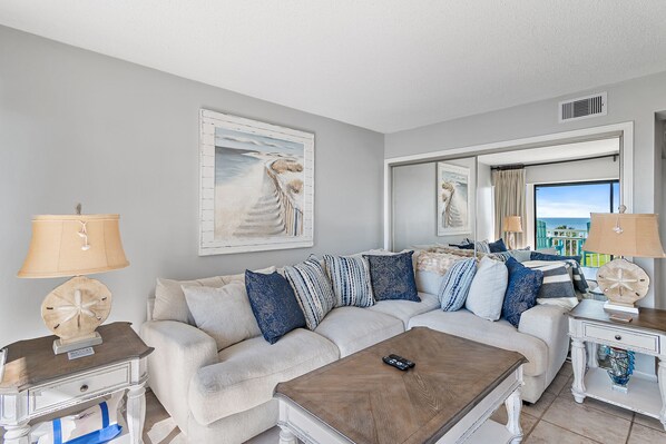 A living room with a beige sectional sofa, a wooden coffee table, and a view of the ocean through a large window. - Beach-side summer escape! (Destin)