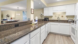 A modern kitchen with white cabinets, granite countertops, and a built-in oven. - Beach-side, beautiful low-rise with uncrowded beach! (Destin)