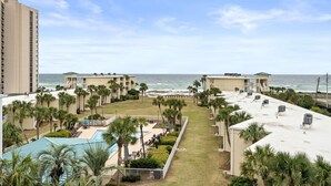 A resort with a pool, palm trees, and a view of the beach and ocean. - Beach-side, beautiful low-rise with uncrowded beach! (Destin)