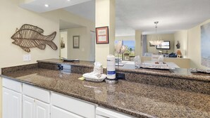 A kitchen with granite countertops, a fish wall art, a framed certificate, and a view of the outdoors. - Beach-side, beautiful low-rise with uncrowded beach! (Destin)
