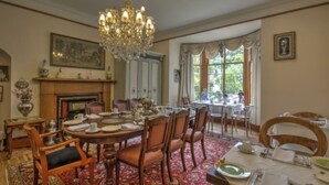 A formal dining room with a chandelier, a fireplace, and a view of greenery through large windows.