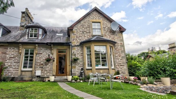 A stone house with a central entrance, a bay window, and a satellite dish.