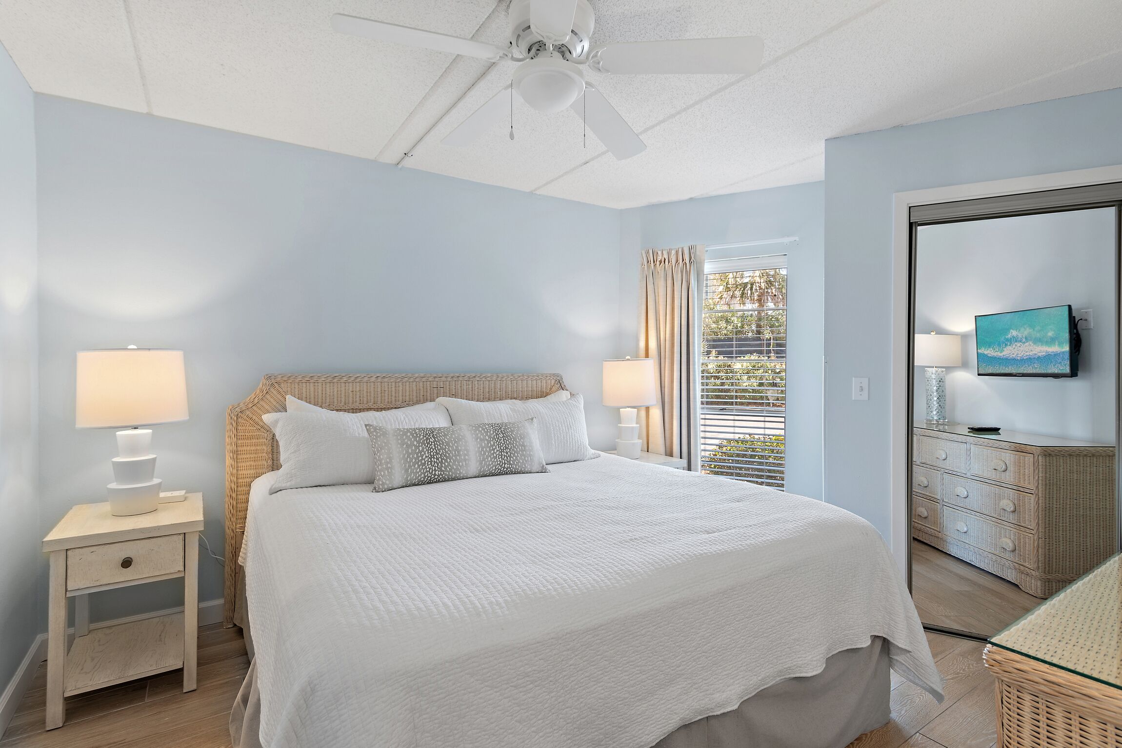 A bedroom with a bed, nightstands, a ceiling fan, a window with curtains, and a TV on a dresser.