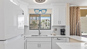 Une cuisine moderne avec des meubles blancs, un lave-vaisselle encastré et une fenêtre équipée de stores.