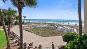 A beach view with palm trees, a sandy area, and a paved walkway. - Beach-side, beautiful low-rise with uncrowded beach! (Destin)