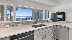 A kitchen with a large window overlooking a beach, a stainless steel sink, and modern cabinetry. - Beach-side, beautiful low-rise with uncrowded beach! (Destin)