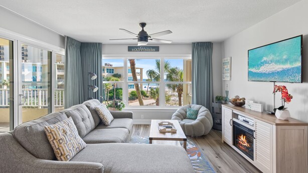 A modern living room with a grey sofa, a coffee table, a fireplace, and a large TV. - Newly updated!! 2 Bed 2 Bath Beach View! (Destin)