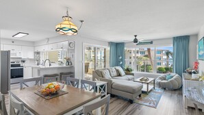 A modern apartment with a kitchen, dining area, and living room. It features a large window with a view of buildings and a balcony. - Newly updated!! 2 Bed 2 Bath Beach View! (Destin)