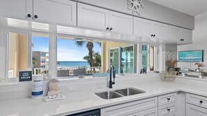 A modern kitchen with white cabinetry, a stainless steel sink, and a view of the ocean. - Newly updated!! 2 Bed 2 Bath Beach View! (Destin)