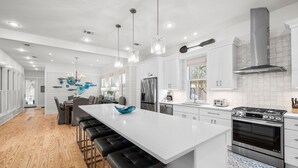 A modern kitchen with white cabinetry, a large island with bar stools, stainless steel appliances, and pendant lighting.