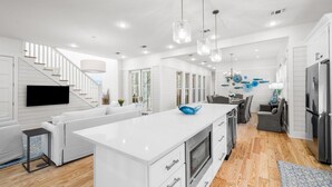 A modern kitchen with white cabinetry, a large island, and a dining area with gray chairs.