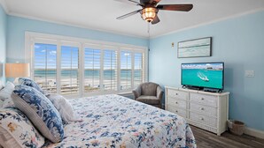 Ein Schlafzimmer mit einem großen Bett, einem Deckenventilator, einem Fernseher und Meerblick durch die Fenster.