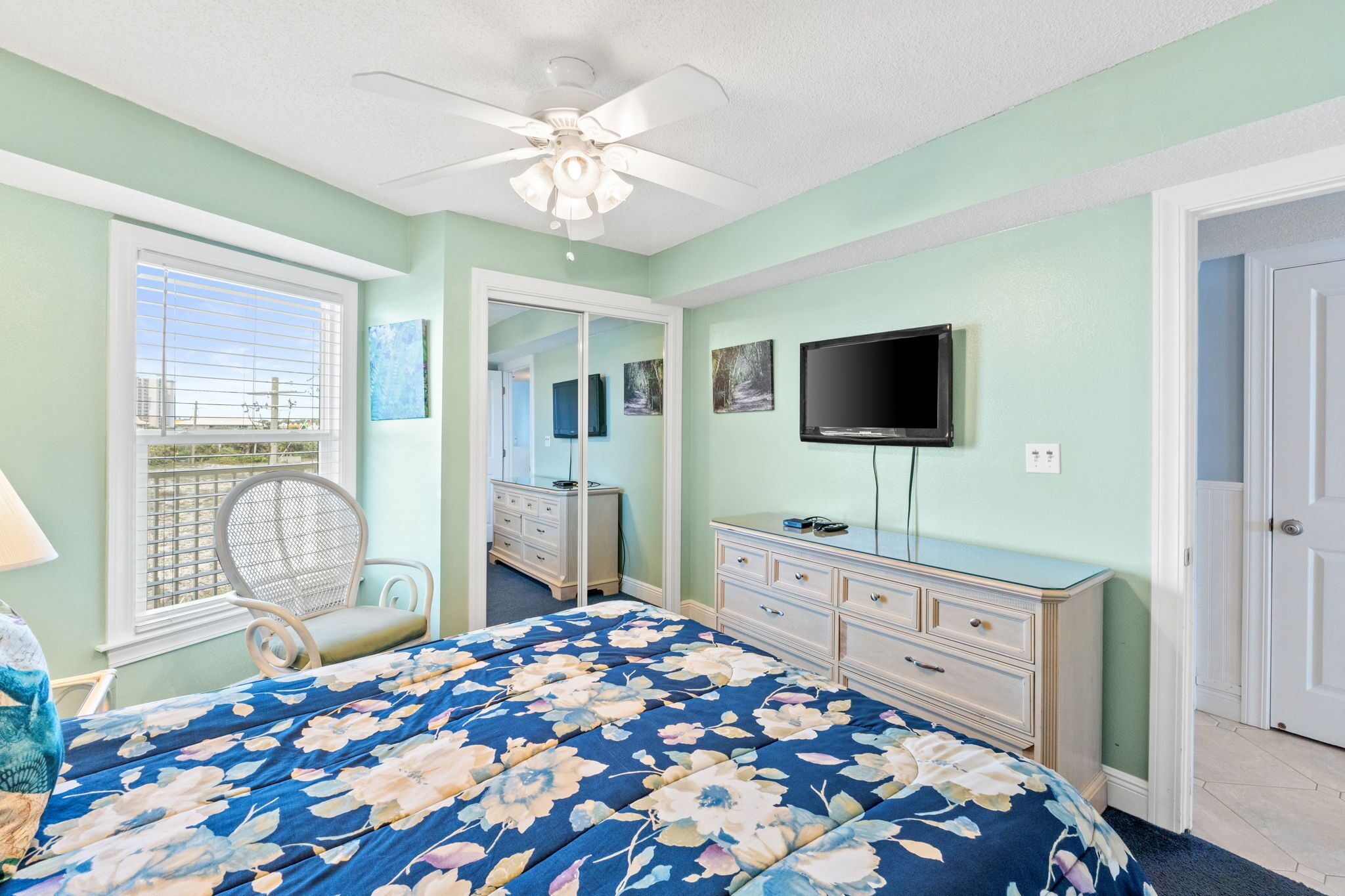 A bedroom with a bed, dresser, television, and a window with blinds.