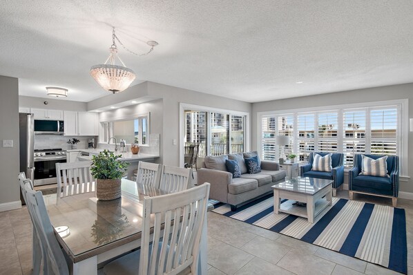 A modern living room with a dining area, a kitchen, and large windows.