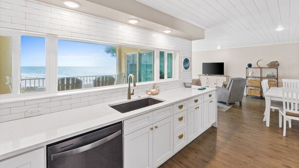 Una cocina moderna con una isla grande, muebles blancos y vistas al océano.